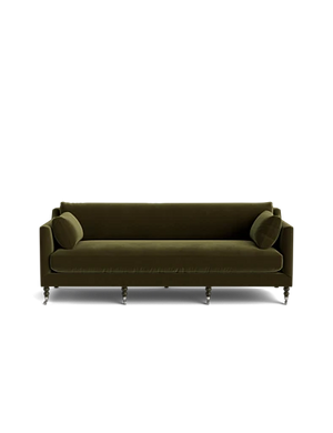 The Fabienne Sofa, in a luxurious green velvet, comes with two matching round pillows. It features a classic design and wooden legs, all showcased against a plain black background.