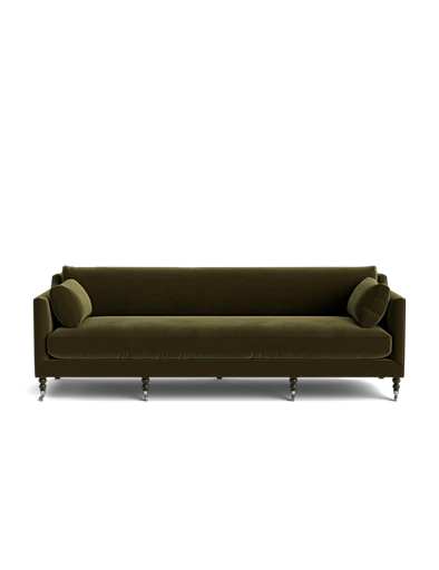 The Fabienne Sofa is upholstered in dark green velvet, featuring rounded armrests and accompanied by two matching cylindrical cushions. Its sleek metallic legs add a touch of modern elegance and comfort against a plain black background.