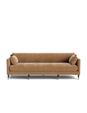 The Fabienne Sofa, featuring a brown upholstered design with wooden legs and two matching cylindrical pillows on either side, is set against a plain white background.