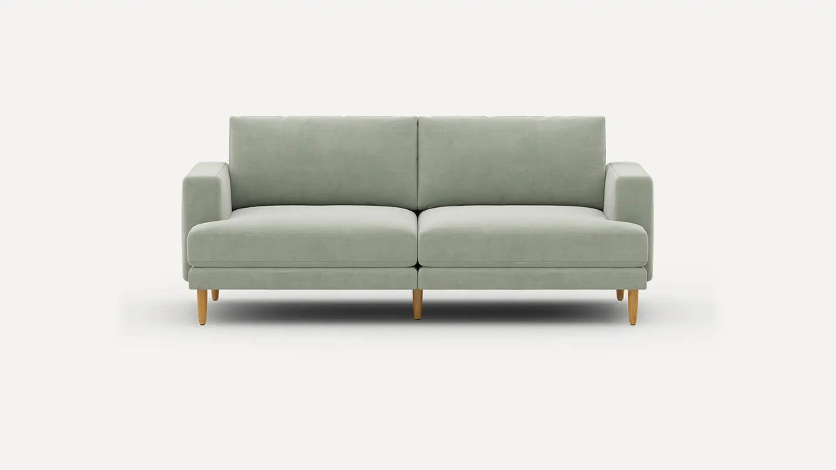 The Ember Mid-Century Modern 75" Sofa is showcased against a plain white background, highlighting its minimalist and contemporary design with a light green color, clean lines, and wooden legs. It includes two seat cushions and two back cushions for added comfort.