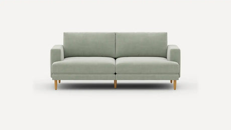The Ember Mid-Century Modern 75" Sofa is showcased against a plain white background, highlighting its minimalist and contemporary design with a light green color, clean lines, and wooden legs. It includes two seat cushions and two back cushions for added comfort.
