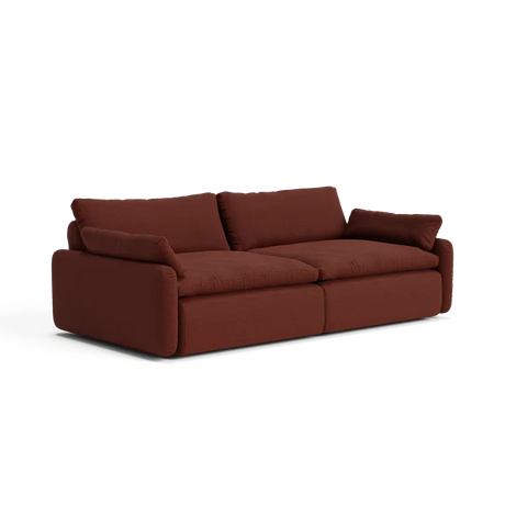 The Sink Down Sectional is a plush sofa in a deep red shade, featuring soft cushions and wide armrests. Its contemporary design and cozy, inviting appearance make it perfect for a modern living room.