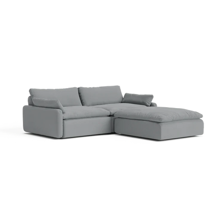 The Sink Down Sectional is a sleek and minimalistic gray sectional sofa with plush cushions, featuring a chaise on the right side, perfect for a contemporary living room setting.