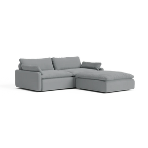 The Sink Down Sectional is a sleek and minimalistic gray sectional sofa with plush cushions, featuring a chaise on the right side, perfect for a contemporary living room setting.