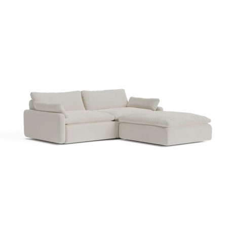 The Sink Down Sectional is a modern, light beige sofa with plush cushions and a left-hand chaise lounge. It boasts a minimalist design and embodies both comfort and elegance.