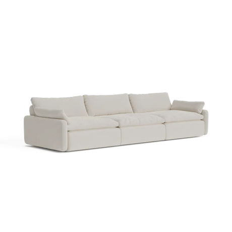 A contemporary, beige three-seater sectional named "The Sink Down Sectional" featuring plush cushions and a minimalist design, set against a white backdrop.