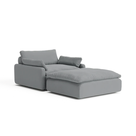 Introducing The Sink Down Sectional, a contemporary gray sectional perfectly paired with an ottoman, showcasing plush cushioning and a sleek, minimalist design against a pristine white backdrop.