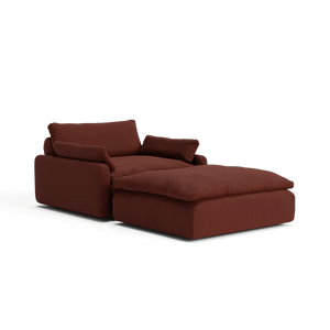 The Sink Down Sectional is a plush, burgundy armchair that includes an attached ottoman, featuring deep cushions and a block-style design. This chair provides a comfortable and modern aesthetic, making it ideal for lounging in any living space.