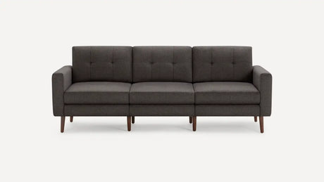 The Nomad Fabric Sofa, a modern three-seater in dark gray with square cushions and wooden legs, is showcased against a plain white background. It boasts clean lines and a minimalist design.