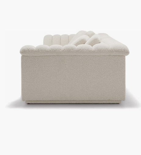 Side view of the cream-colored Float Sofa, featuring a modern design with a low, tufted back and armrest. The soft and textured upholstery is set against a plain white background.