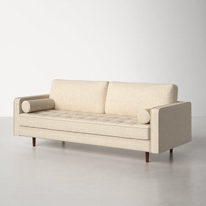 A contemporary Geo 84'' Upholstered Sofa in beige, showcasing geometric armrests and cylindrical pillows, with tufted cushions and wooden legs, styled against a light gray backdrop.