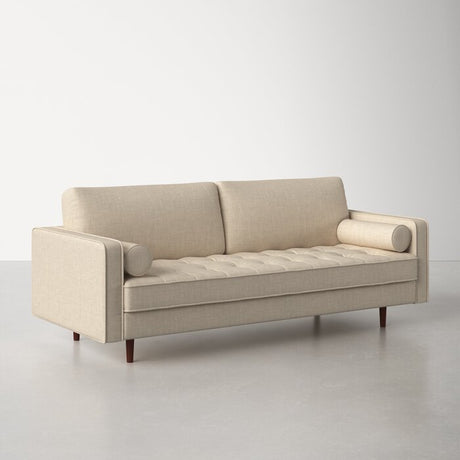 The Geo 84'' Upholstered Sofa in beige, featuring tufted cushions, cylindrical arm pillows, and wooden legs, is showcased on a light gray floor with a white background.