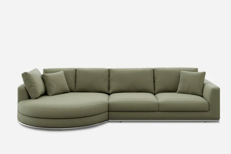 A modern green sectional sofa with a curved chaise lounge on the left. It features three seat cushions and four matching throw pillows. The sofa is set against a plain white background.