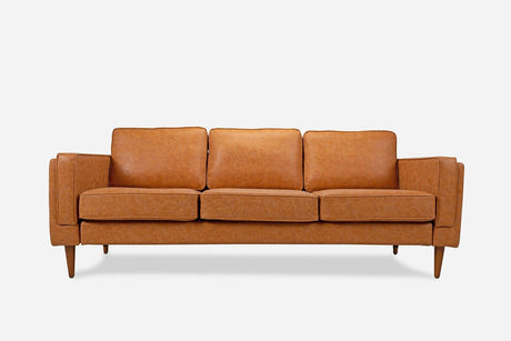 The Albany Sofa, featuring a mid-century modern design in warm tan vegan leather, has three cushioned seats and wooden legs, set against a plain white background.