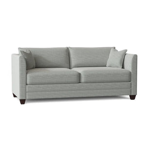 The Kodie 76.5" Upholstered Sleeper Sofa features a light gray fabric, complemented by two matching cushions. Its slim armrests and dark wooden legs add to the modern and minimalist aesthetic.