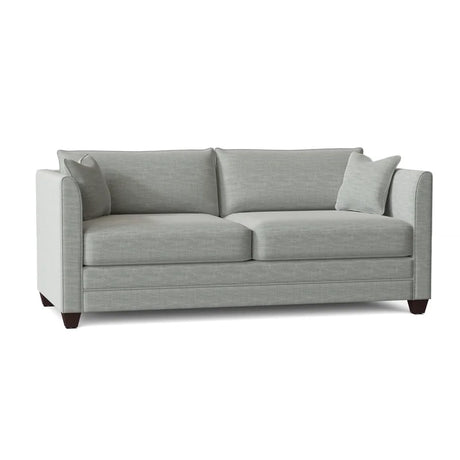 The Kodie 76.5" Upholstered Sleeper Sofa features a light gray fabric, complemented by two matching cushions. Its slim armrests and dark wooden legs add to the modern and minimalist aesthetic.