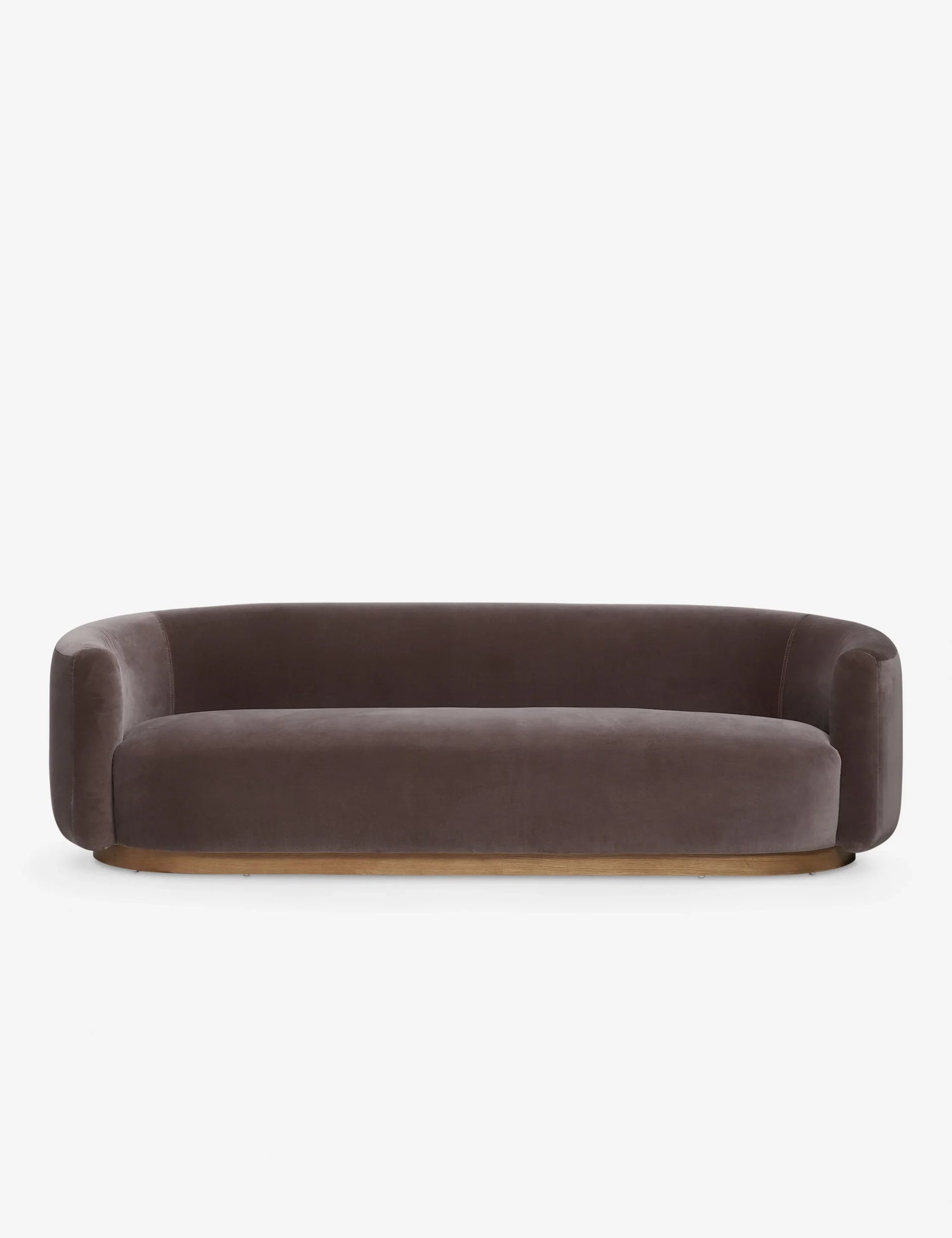 The Lowry Sofa is a stylish piece with its dark gray velvet upholstery, rounded arms, and low backrest. Set against a plain white background, it boasts a sleek, minimalist design with a wooden base that gives it an elegant and contemporary appearance.