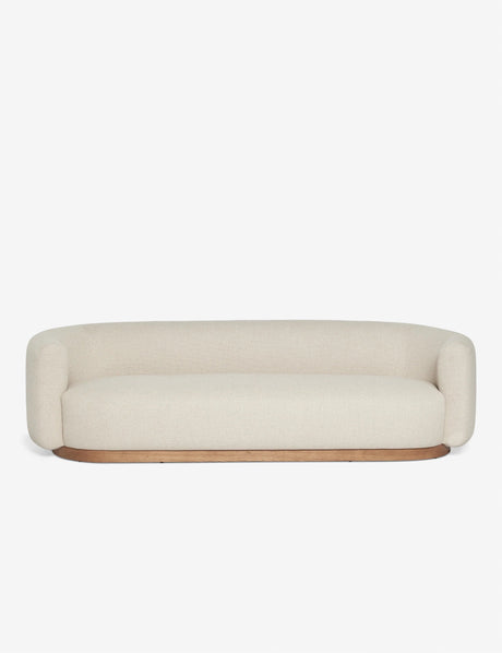 The Lowry Sofa is a modern and minimalist beige piece, featuring rounded edges and a sleek wooden base, set against a plain white background.