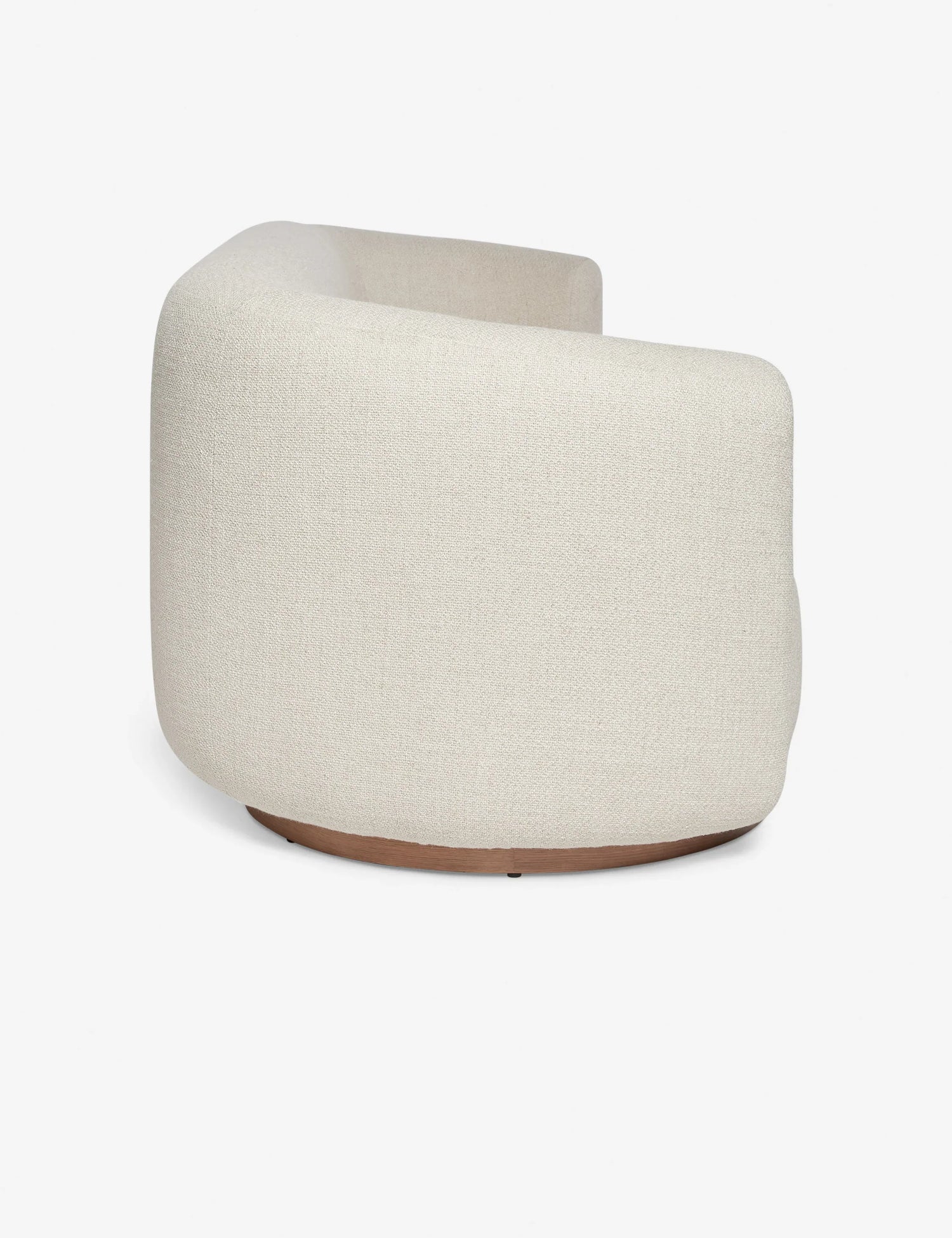 Side view of a contemporary, rounded beige fabric Lowry Sofa featuring a sleek wooden base against a plain white background. The sofa boasts a minimalist design and an upholstered texture.