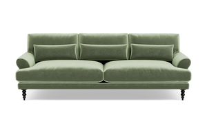 The Maxwell Custom Sofa is a green velvet piece featuring three back cushions, two seat cushions, and a pair of armrests. It comes with four small decorative pillows and rests on four dark wooden legs that give it a classic and elegant appearance.