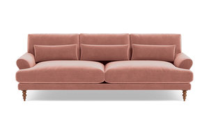 The Maxwell Custom Sofa is a plush, pink velvet piece featuring three back cushions and four cylindrical accent pillows. It showcases rolled arms and is supported by turned wooden legs, offering a blend of classic and contemporary design.
