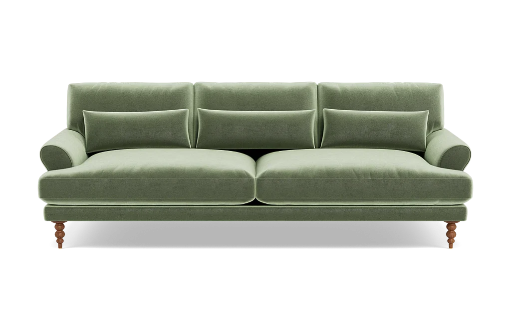 The Maxwell Custom Sofa, upholstered in green velvet, features three seat cushions and matching backrests. It comes with three rectangular pillows and has elegantly rounded armrests. The sofa is supported by four wooden legs, blending a classic touch with its modern design.