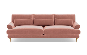 Introducing the Maxwell Custom Sofa: a charming pink velvet piece featuring three seat cushions and coordinating back cushions. It boasts elegantly rounded armrests and stands on four wooden legs adorned with intricate carvings. Enhancing its comfort are two rectangular throw pillows on the seat, all set against a simple black backdrop.