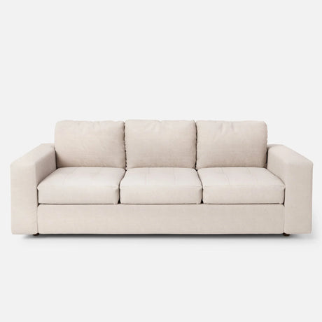 The Marc Tufted Sofa, a beige three-seater with plush cushions and a minimalist design, is set against a plain white background.