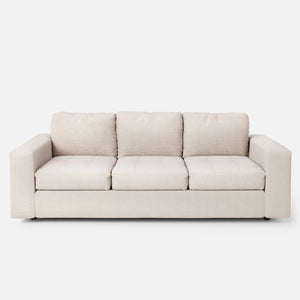 The Marc Tufted Sofa, a beige three-seater with plush cushions and a minimalist design, is set against a plain white background.