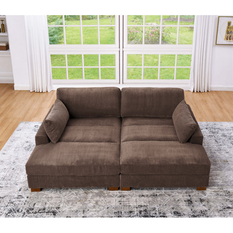 An Etta Avenue Mordecai 90'' Square Arm Sofa in brown corduroy is positioned on a patterned area rug in a living room with wooden floors. Large windows in the background reveal a green, grassy outdoor view, framed by white curtains.