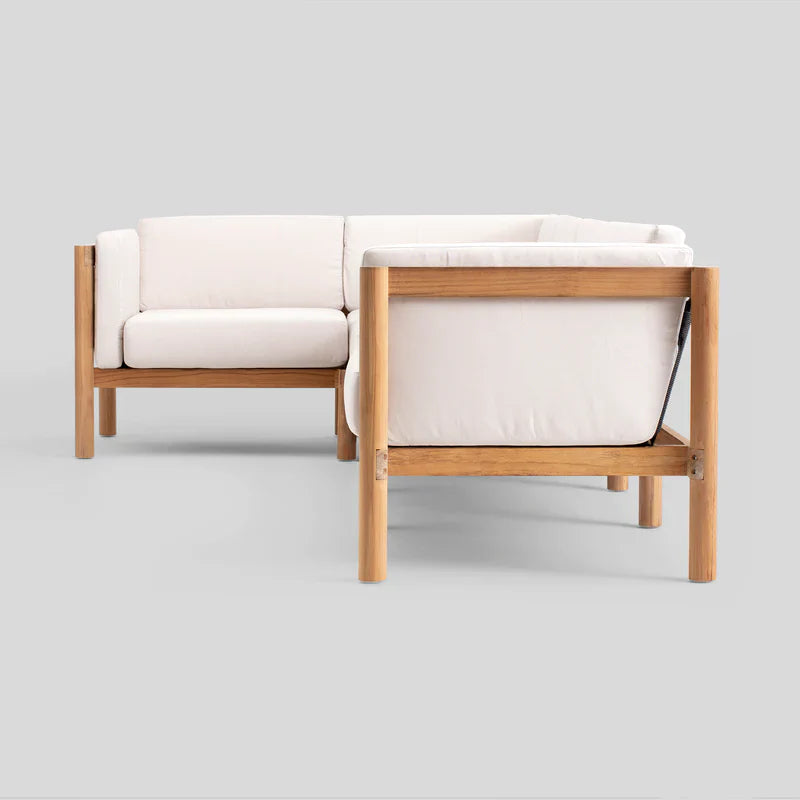 The Haven Sectional is a modern L-shaped sofa featuring an elegant wooden frame and off-white cushions. Its sleek, minimalist design makes it perfect for contemporary interiors, as seen against a plain gray background.