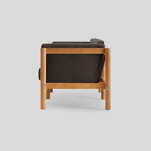 A side view of the Haven Sofa, featuring a minimalist wooden frame and dark cushions, set against a light gray background. The sofa showcases a modern design with clean lines and light wood.