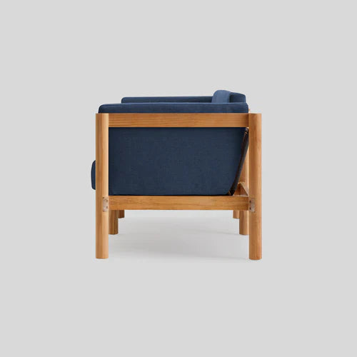 Side view of the Haven Sofa, a modern piece in blue with a wooden frame, set against a light gray background. The design showcases clean lines and a minimalist aesthetic.