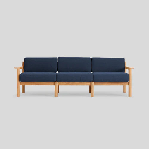 The Haven Sofa is a contemporary three-seater featuring a wooden frame and dark blue cushions set against a light gray backdrop. Its minimalist design showcases straight lines without any visible patterns.