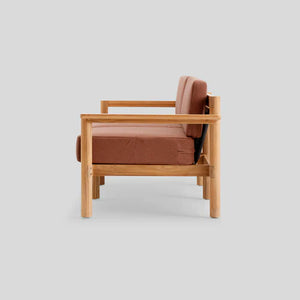 Side view of the Haven Sofa featuring a wooden frame with a rust-colored cushion and backrest, set against a plain gray background. The sofa boasts a minimalist, modern design.