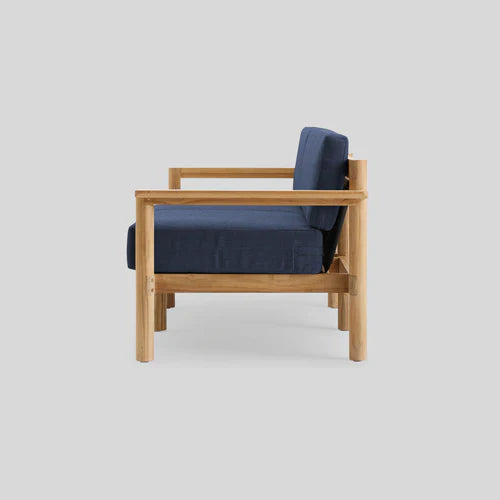 Side view of the Haven Sofa, featuring a minimalist design with a light wood frame and navy-blue cushions on both the seat and backrest. The background is a solid gray.