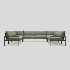 The Terra Sectional is a green L-shaped sofa featuring a sleek metal frame and plush cushions, set against a light gray background. Its minimalist design boasts straight lines and offers comfortable seating for multiple people.