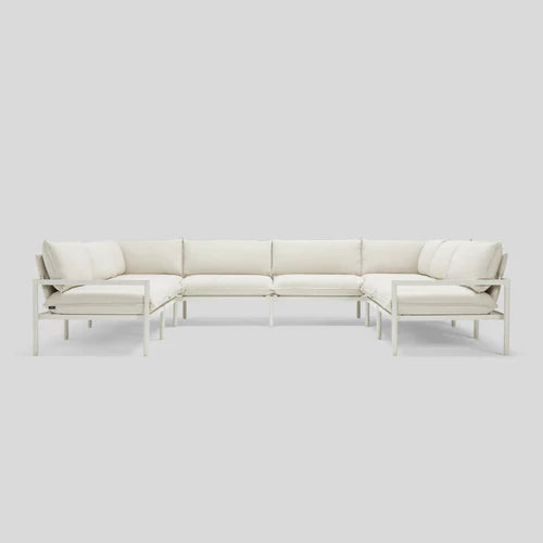 The Terra Sectional, a minimalist L-shaped white sofa, is displayed against a light gray background. It boasts clean lines, a metal frame, and plush cushions for a modern and contemporary appearance.