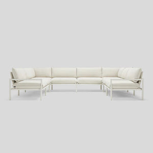 The Terra Sectional, a minimalist L-shaped white sofa, is displayed against a light gray background. It boasts clean lines, a metal frame, and plush cushions for a modern and contemporary appearance.