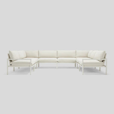 The Terra Sectional, a minimalist L-shaped white sofa, is displayed against a light gray background. It boasts clean lines, a metal frame, and plush cushions for a modern and contemporary appearance.