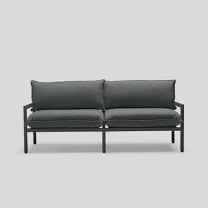 Introducing the Terra Loveseat: a minimalist outdoor sofa in dark gray, featuring a sleek metal frame and complemented by two cushioned seats and backrests, displayed against a simple light gray backdrop.