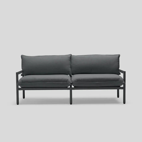 Introducing the Terra Loveseat: a minimalist outdoor sofa in dark gray, featuring a sleek metal frame and complemented by two cushioned seats and backrests, displayed against a simple light gray backdrop.