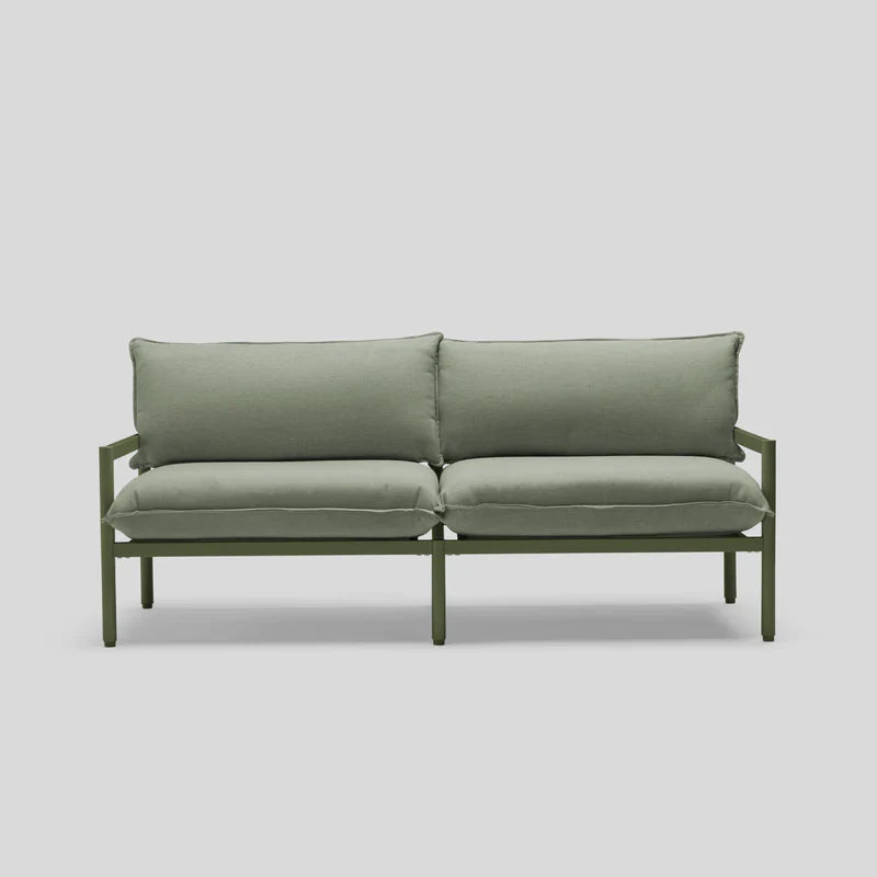 The Terra Loveseat is a minimalist green sofa featuring two seat cushions and two back cushions, all supported by a sleek metal frame, set against a light gray background.