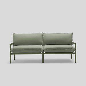 The Terra Loveseat is a minimalist green sofa featuring two seat cushions and two back cushions, all supported by a sleek metal frame, set against a light gray background.