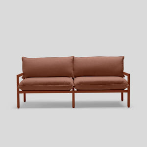 The Terra Loveseat, a minimalist piece with a wooden frame, is set against a gray backdrop. It features two seat cushions and two back cushions, providing a simple and modern design.