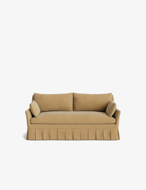 Introducing the Portola Pleated Sofa: a tan-colored, three-seater with a skirted base and two matching cylindrical cushions on either side. This sofa boasts a minimalist design, beautifully showcased against a plain white background.