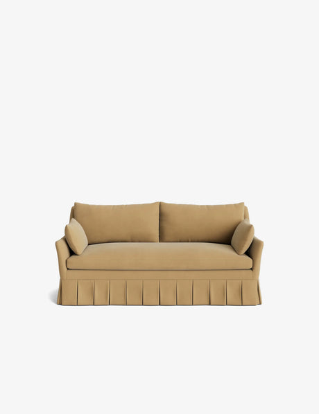 Introducing the Portola Pleated Sofa: a tan-colored, three-seater with a skirted base and two matching cylindrical cushions on either side. This sofa boasts a minimalist design, beautifully showcased against a plain white background.