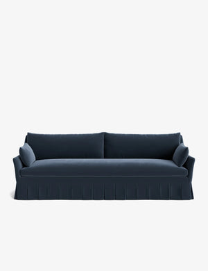 The Portola Pleated Sofa is a sleek, dark blue piece with a pleated skirt, featuring two back cushions and two bolster pillows on each end, all set against a plain white background.