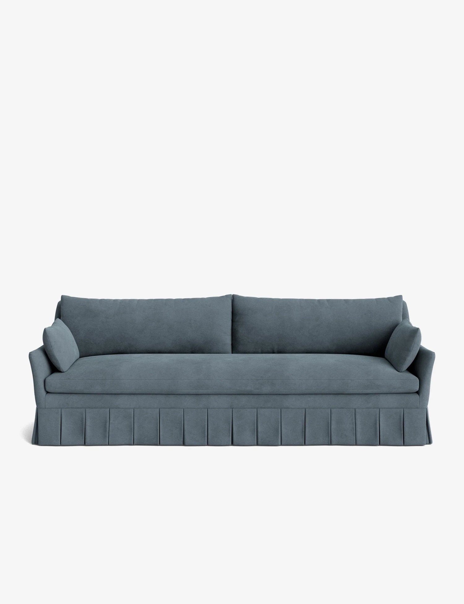 The Portola Pleated Sofa, in a teal velvet finish, showcases pleated skirt detailing, two large back cushions, and two cylindrical side pillows, all set against a plain white background.