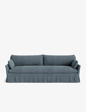 The Portola Pleated Sofa, in a teal velvet finish, showcases pleated skirt detailing, two large back cushions, and two cylindrical side pillows, all set against a plain white background.